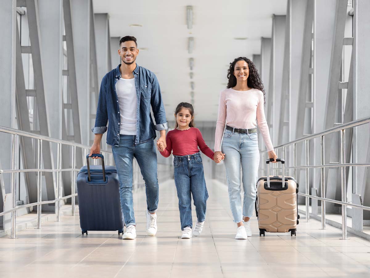 a young family with parents either side of a child pulling luggage in an airport