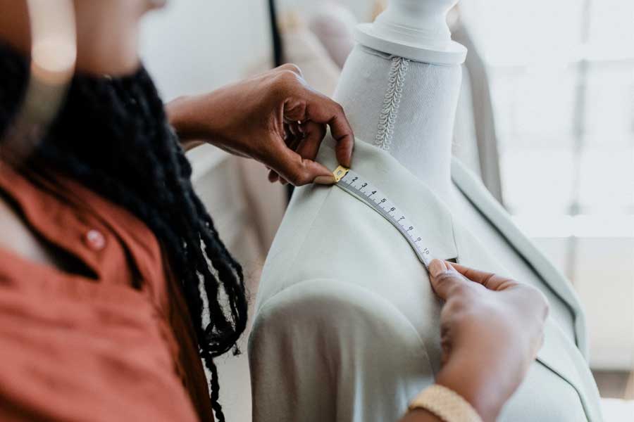 A person holding a tape measure on a dressmakers dummy