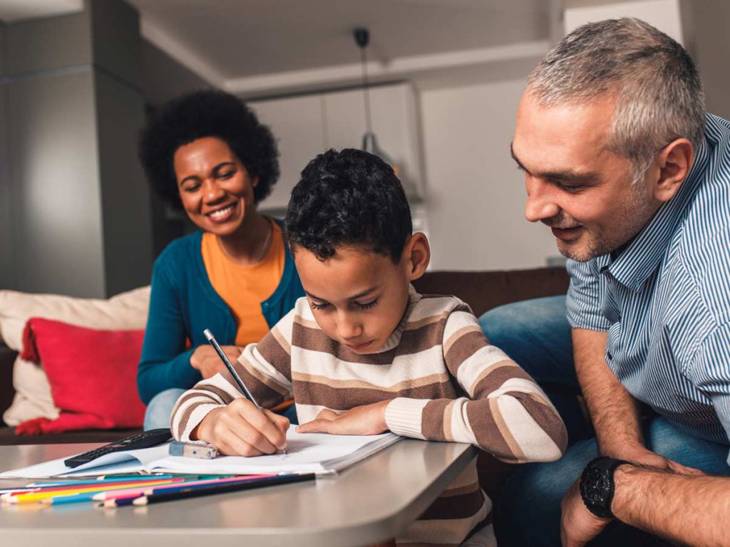 A boy writing in an exercise book with his parents watching him