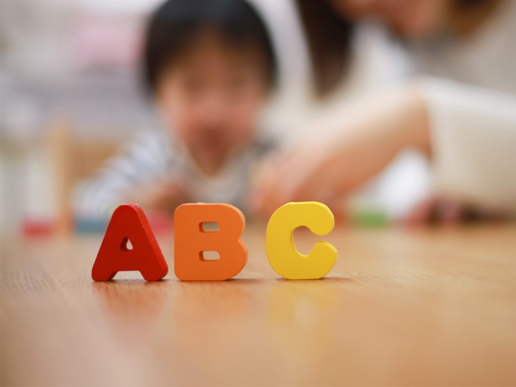 The letters A, B and C in the foreground with a child and parent blurred in the background