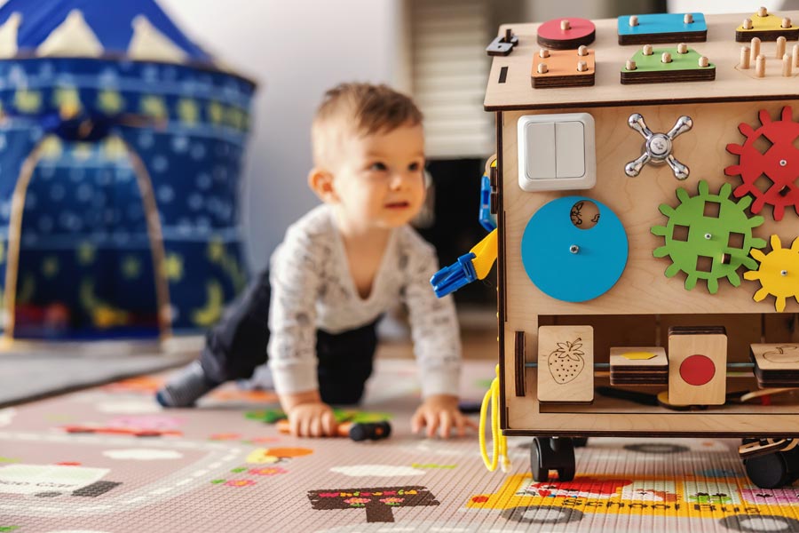 Image of child looking at a large wooden play box with cogs and wheels on it