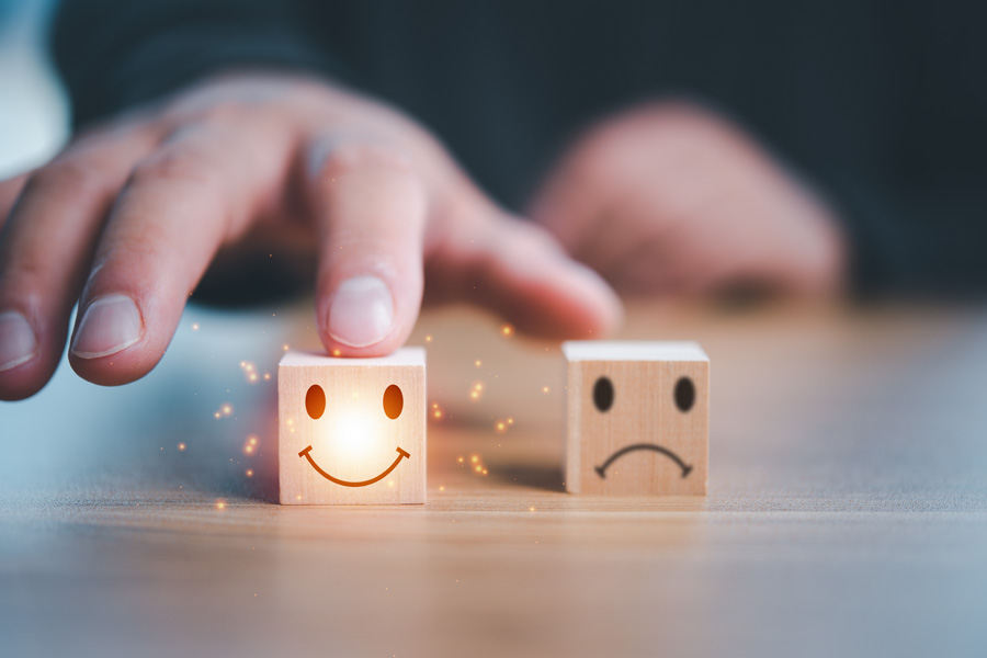 image of two wooden blocks, one with a sad face, the other with a happy face and the finger of a hand on it denoting good customer service.